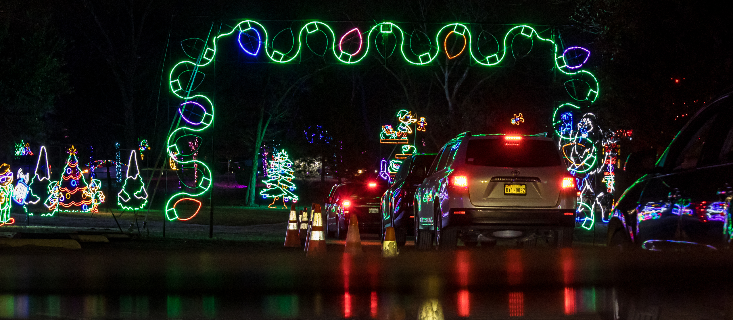 Cars driving under a lit garland arch through the Christmas displays at Lights of Joy in Branson, MO